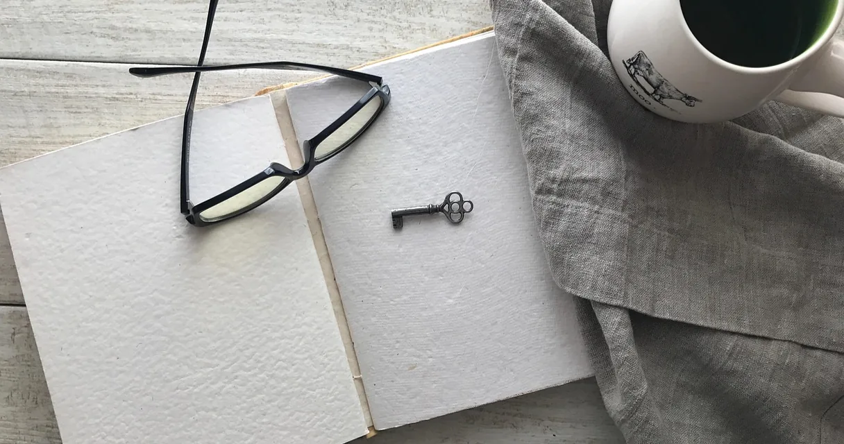 Caderno aberto com óculos de leitura, uma chave pequena e uma xícara de café, ilustrando como funciona o IPTV Plus